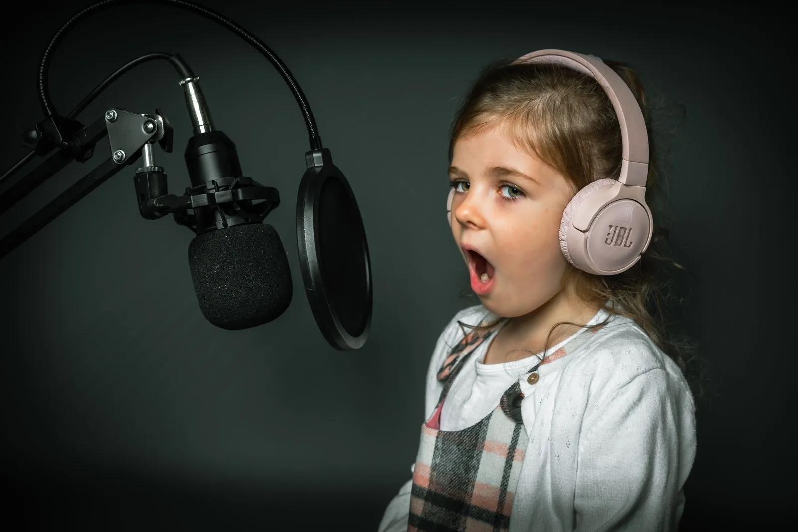 A young girl in a recording studio sings into a microphone wearing headphones.